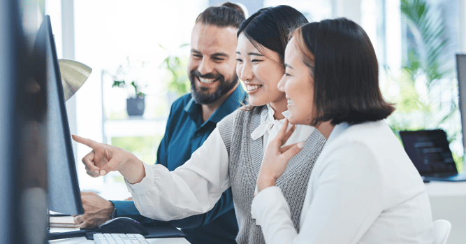 A team of smiling professionals looking at a computer screen.