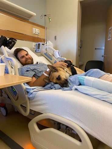 man laying in hospital bed with dog